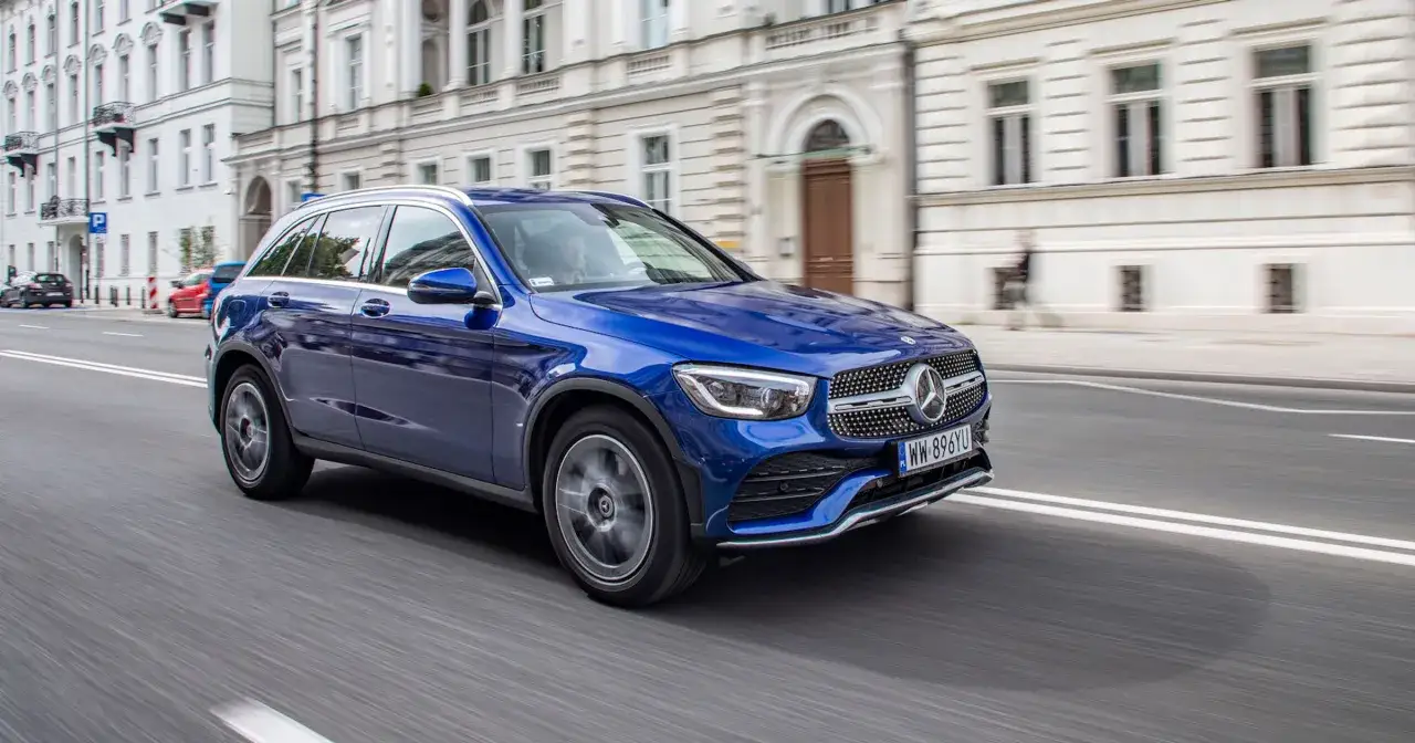 Błękitny Mercedes GLC 200 sunie miejską ulicą. Elegancki SUV z charakterystyczną kratką i reflektorami.