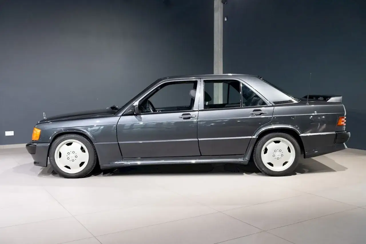 Szary Mercedes 190 z charakterystycznym spoilerem i białymi felgami, gotowy na sportowe wyzwania.