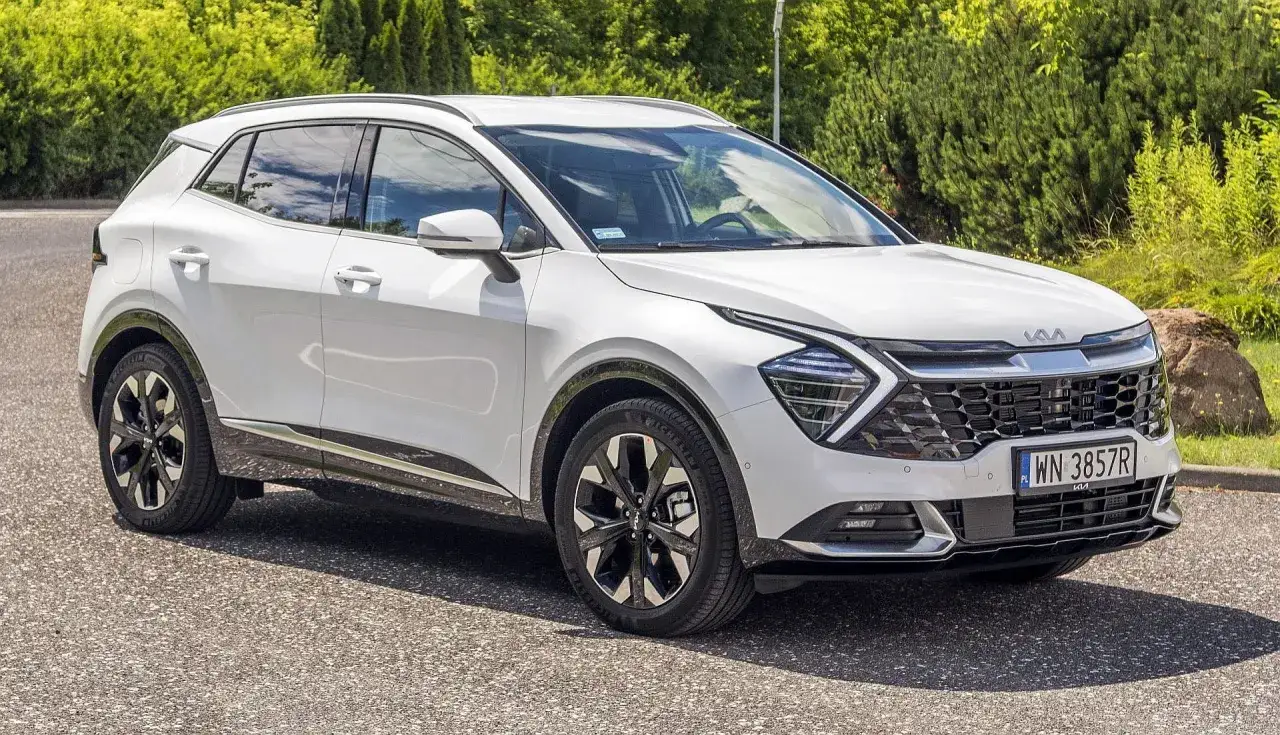 Biały Kia Sportage 1.6 benzyna zaparkowany na tle zieleni. Nowoczesny design i eleganckie felgi.