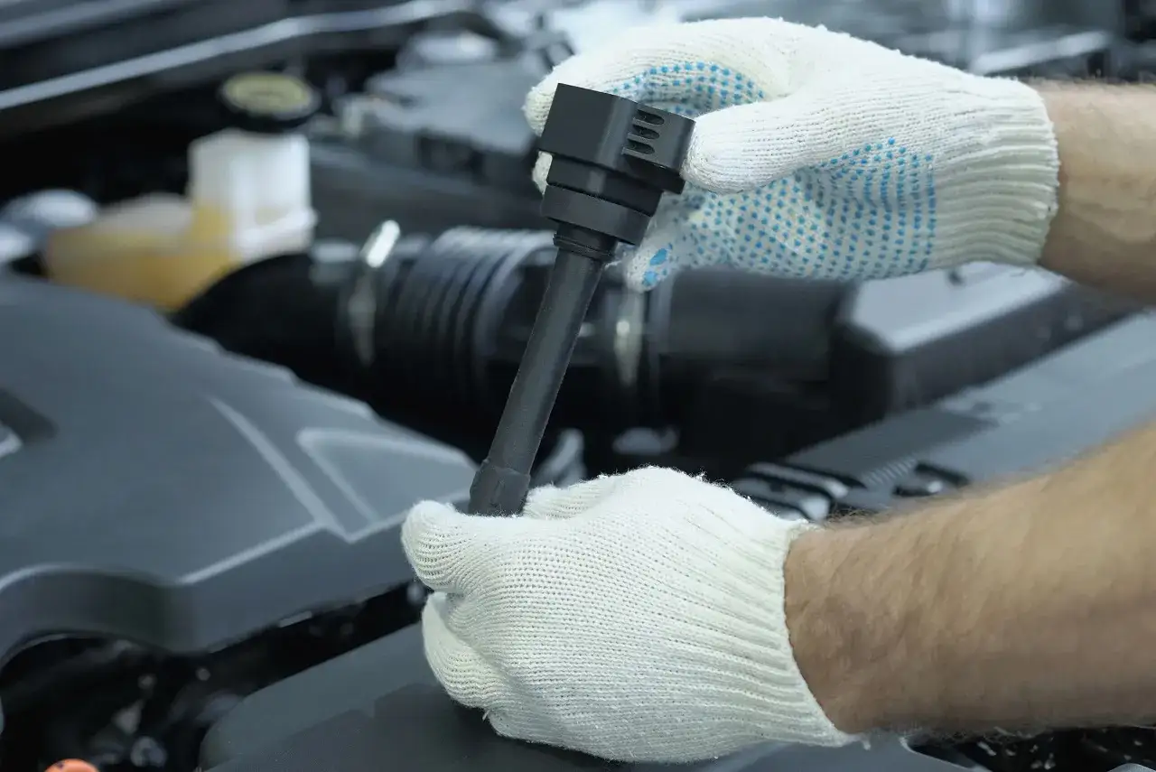 Mechanik w białych rękawiczkach trzyma cewkę zapłonową. Jej wymiana może być konieczna, gdy pojawią się objawy awarii.