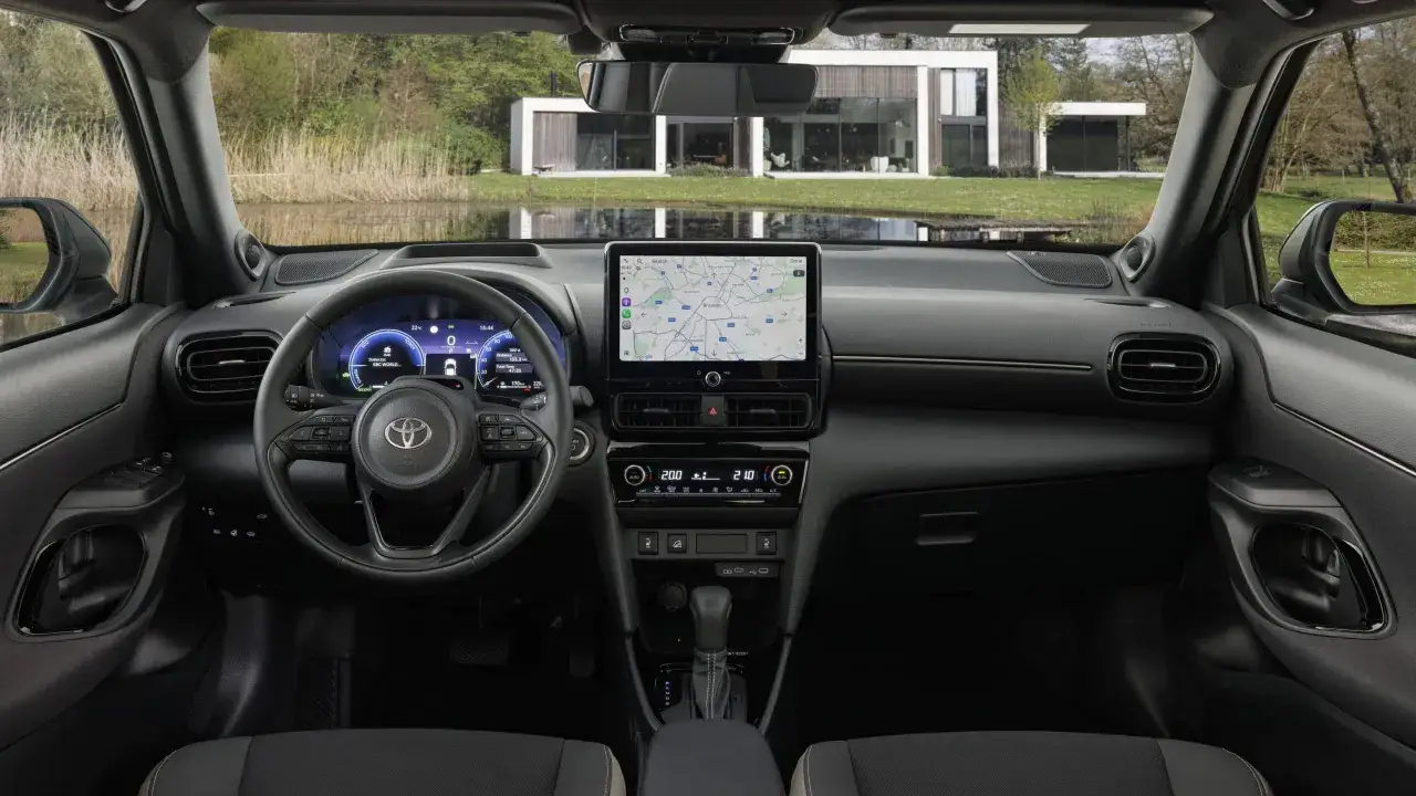 Wnętrze nowoczesnego mini SUV-a z ekranem nawigacji pokazującym trasę do Brukseli. Za oknem piękny widok na dom i jezioro.