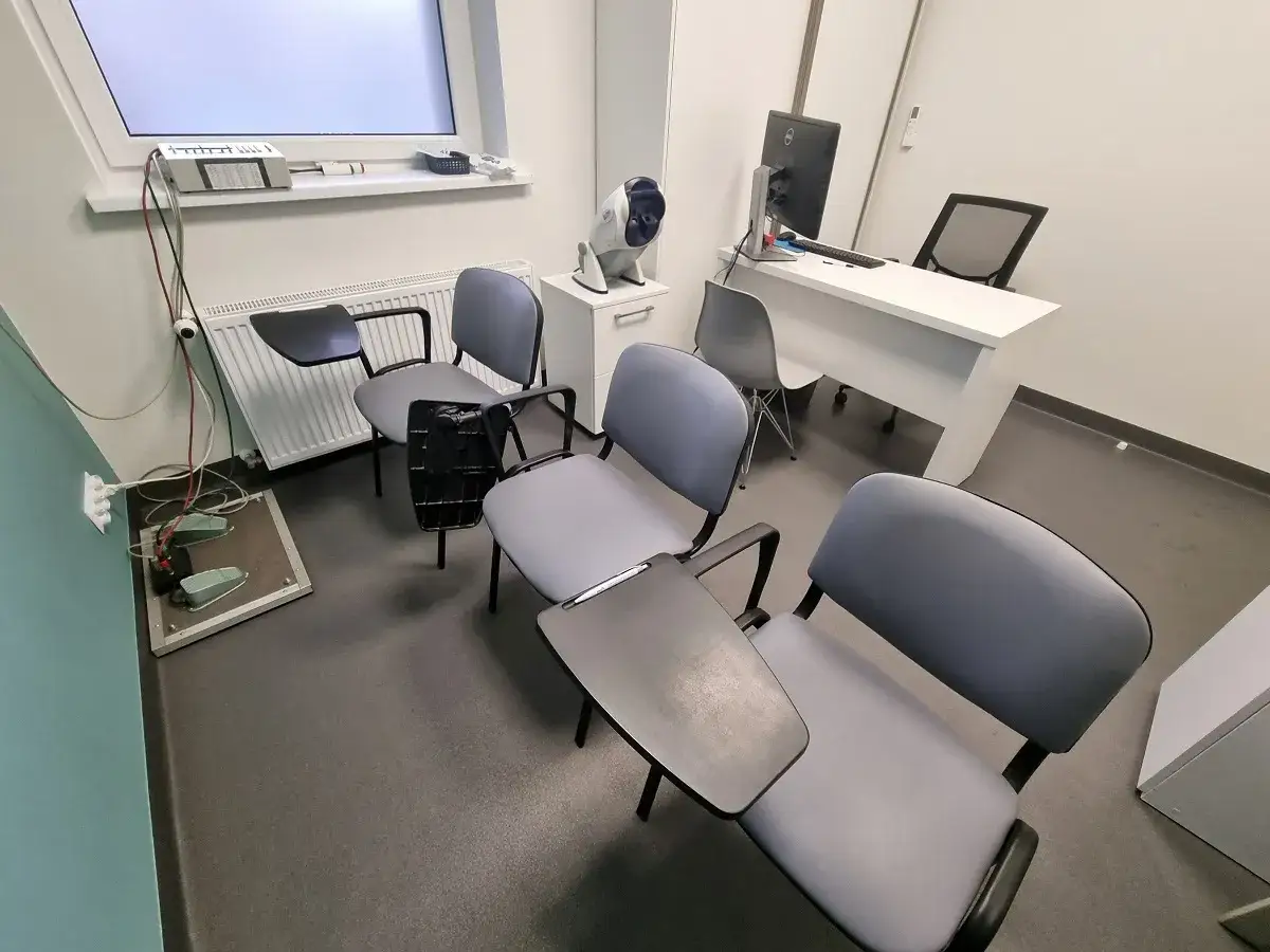 Poczekalnia na testy psychologiczne dla kierowców. Krzesła z podłokietnikami i stolikami, sprzęt do badań.