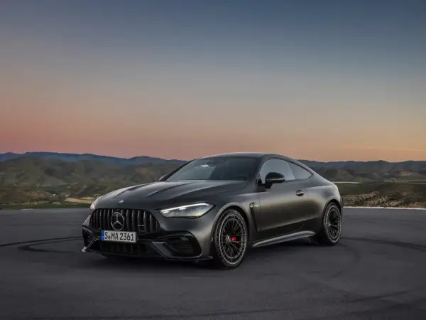 Mroczny Mercedes-AMG GT Coupe na tle zachodzącego słońca i pagórków.